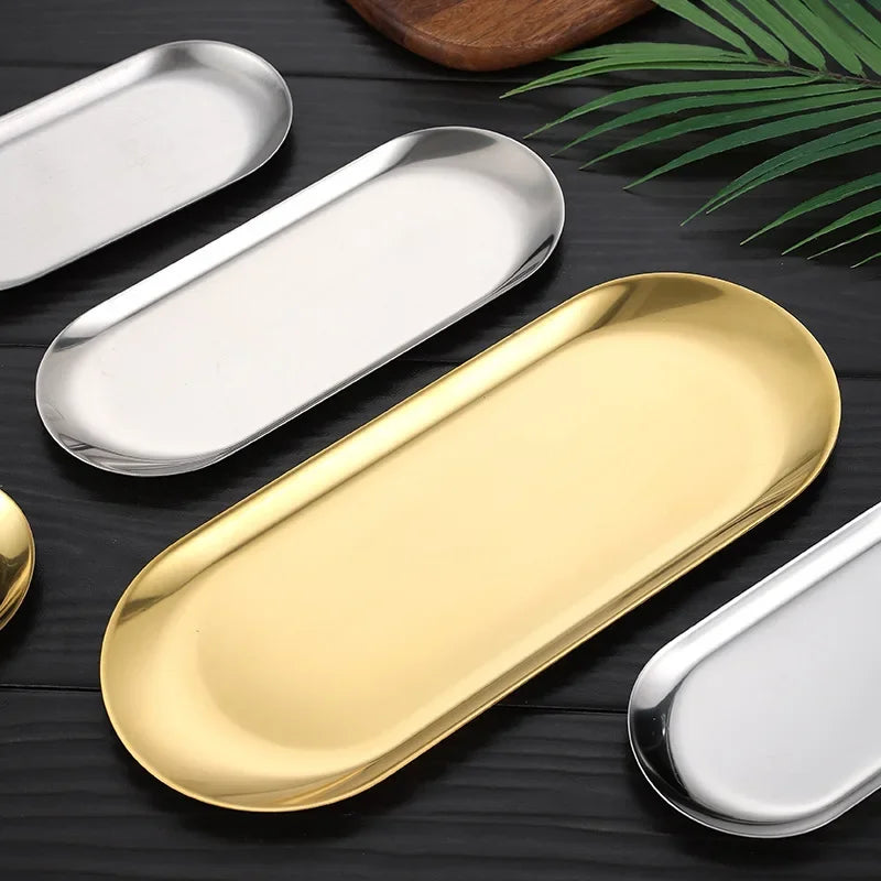 Set of oval metal trays in gold, silver, and white on a dark surface with green leaves.