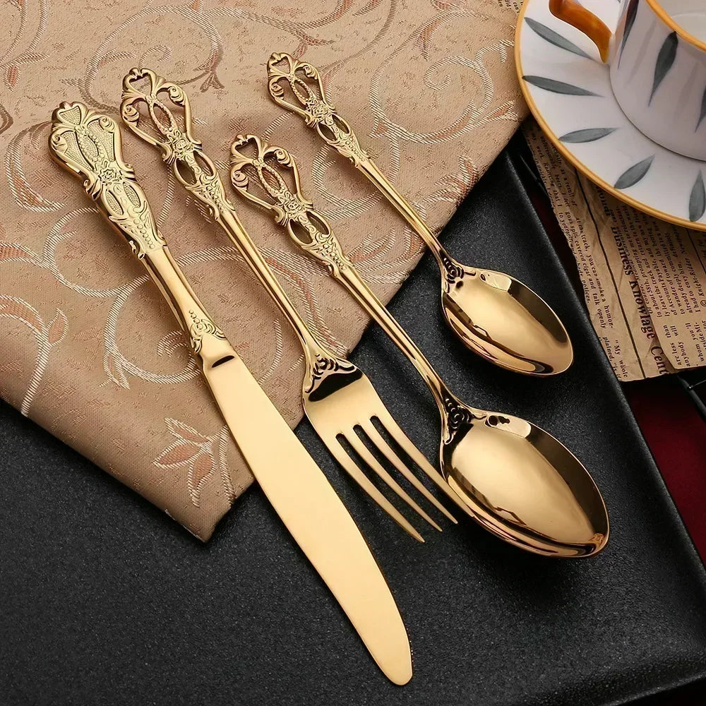 Set of gold cutlery including knife, fork, and spoons on a dark surface with a patterned napkin.