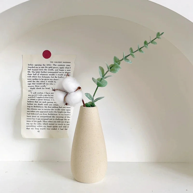 White vase with cotton and a branch on a white surface with a white background