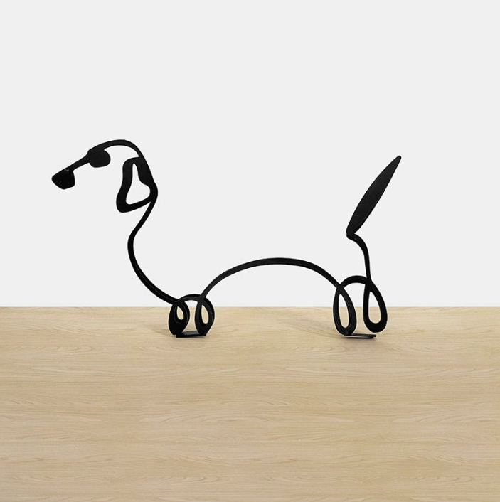 Wire dog sculpture on a wooden surface with a white background