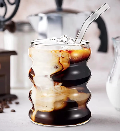 Glass mug with iced coffee and a glass straw, coffee beans and a coffee machine in the background